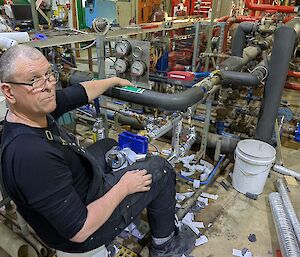 A man sits on a bucket, working in a workshop