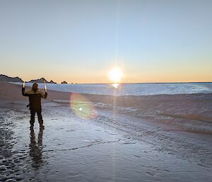 A man in the distance stands on ice, holding up two bits of ice