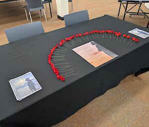 A half circle of poppies on a table with a black tablecloth next to the printed order of service pamphlets