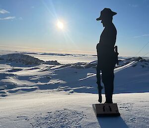 A metal silhouette of a lone soldier standing on the ice with the sun rising in the background