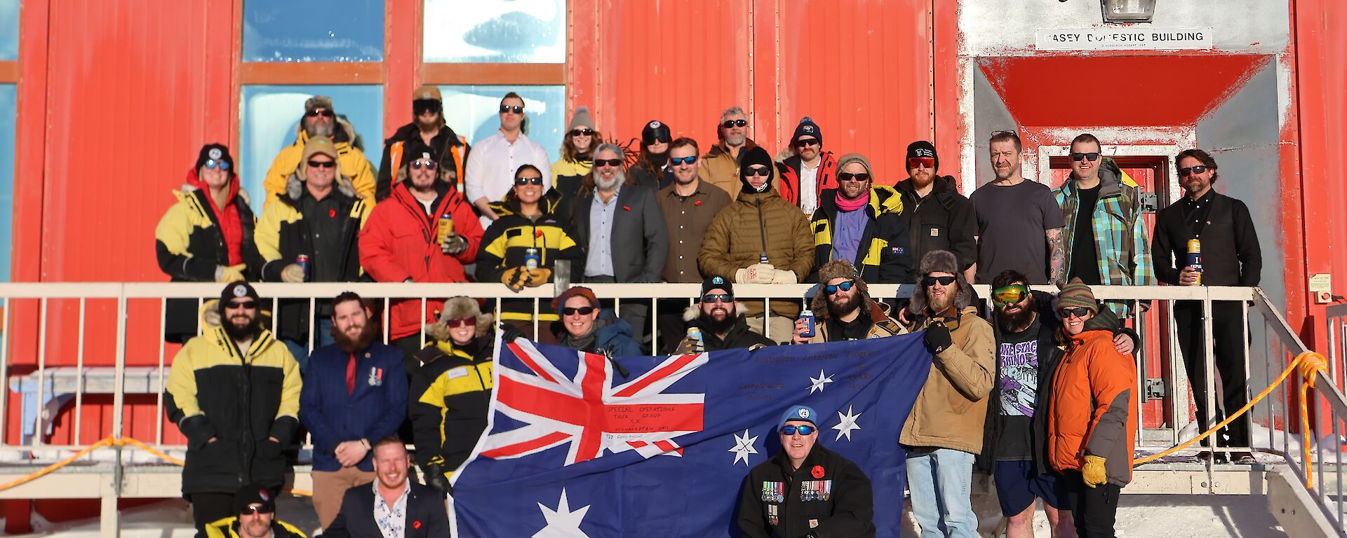 Expeditioners grouped in front of the Red Shed headquarters holding an Australian flag.