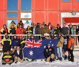 Expeditioners grouped in front of the Red Shed headquarters holding an Australian flag.