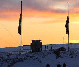 The sun rises over Casey Station showing the ice, the flagpoles and the Casey Station sign