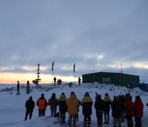 Expeditioners at the dawn service with the flags and ice-mounds in the background.