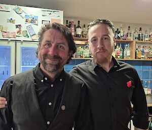 Two expeditioners stand in front of the Casey Station bar on ANZAC Day.