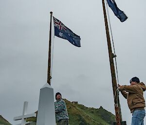 Two people raise Australian flags in front of a white centoph
