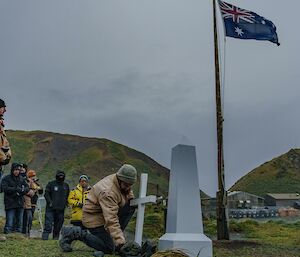 A man lays a poppy on the ground with the station behind him