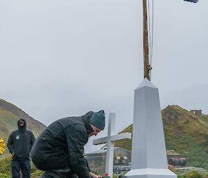 A person lays a poppy down near a white, make-shift cenotaph and white cross, with an Australian flag flying