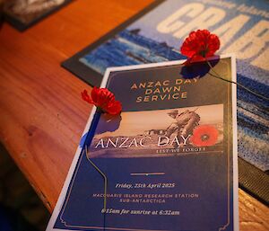 An ANZAC Day service brochure on a table with red poppies next to it