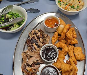 A plate of Chinese food including duck and fried chicken with some small bowls of rice, vegetables and sauce