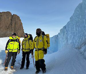 Three expeditioners standing in front of a wall of ice