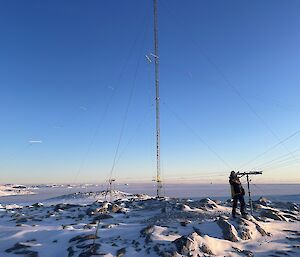 An expeditioner stands on snow covered rocks to repair an antenna in minus 25 degree weather