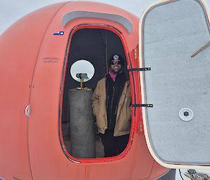 An expeditioner stands inside an orange coloured one-door magnetic observation hut