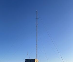 Snow capped rocks on a peak with a hut and an antenna tower with wire cable supports
