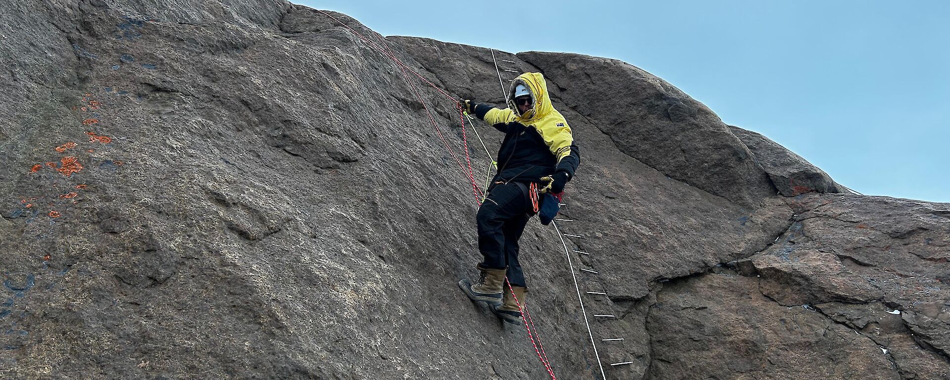 A man climbing up a rope ladder on a big rock