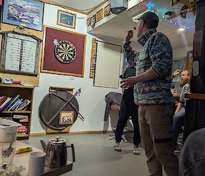 A man in a bright coloured polar fleece lines up to throw a dart