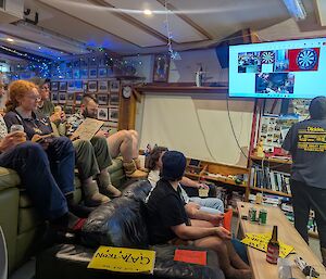 A group of people sit around watching a darts game