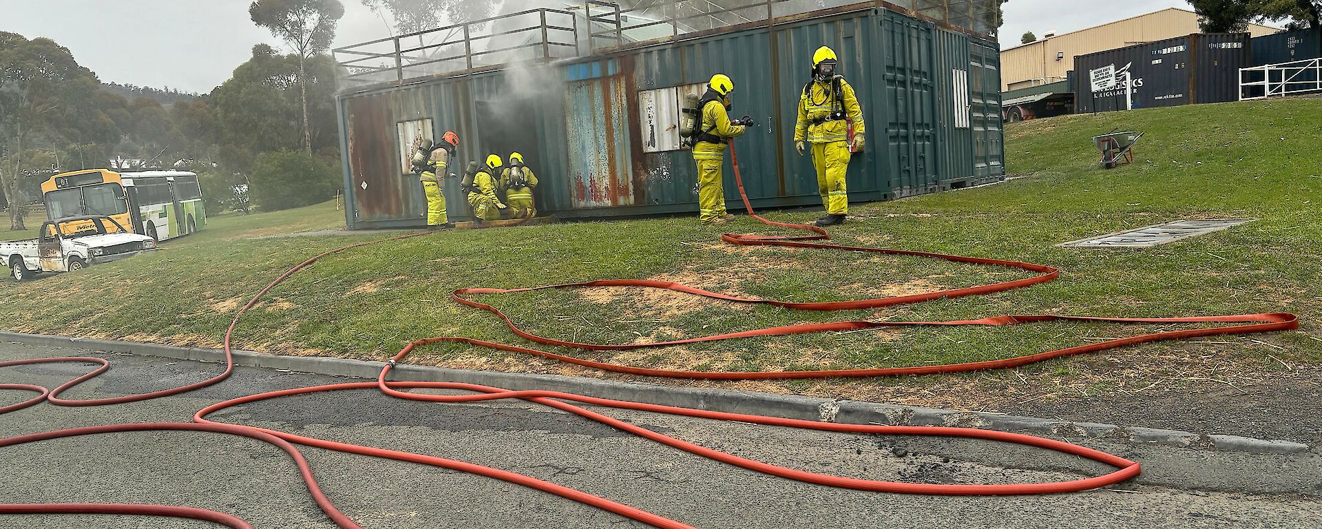 Expeditioners in fire fighting gear; a long hose in the foreground