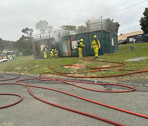 Expeditioners in fire fighting gear; a long hose in the foreground