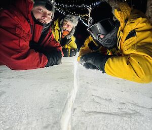 Expeditioners on their stomachs in cold weather clothing facing the camera