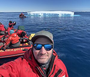 The author in a small boat with an iceberg in the rear picture