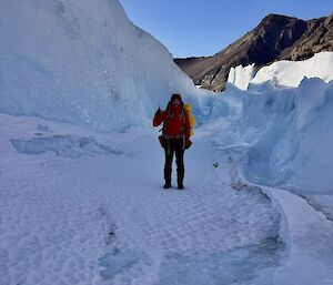 A person walking on ice with a steep ice wall to their right