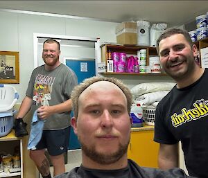 Three men smiling at the camera, one with his hair shaved way back on his forehead