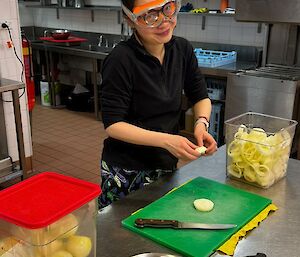 A woman cutting onions in a commercial kitchen wearing swimming goggles