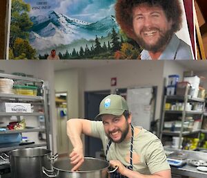 A man in a t-shirt and cap, stirring a big silver pot