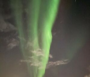 A bright green aurora with three vertical stripes set against the dark night sky with some white clouds visible.