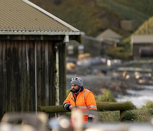 A man in an orange coat leans on a fence and looks into the distance.