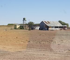A dry outback station with a rusty-roofed homestead, a water tank on a tower and a horse float.