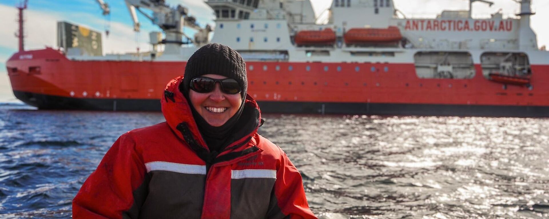 An expeditioner in a small boat, in front of an ice breaker in Antarctica