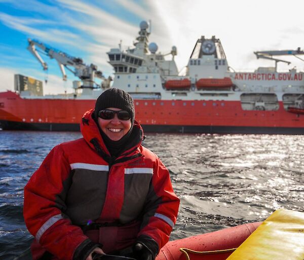 An expeditioner in a small boat, in front of an ice breaker in Antarctica
