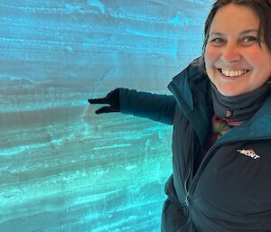An expeditioner in a snow pit in Antarctica, with layers of ice and snow in the background.