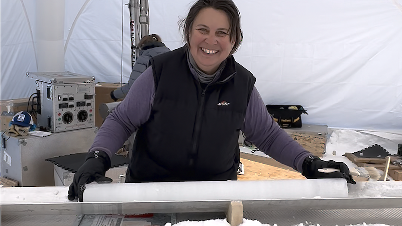 A scientist in Antarctica, holding an ice core in a white drilling tent.