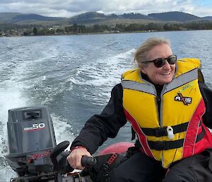 A smiling woman wearing a life jacket steers an inflatable rubber boat