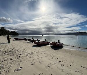 Three inflatable rubber boats sitting on a beach with flat water and sunny sky behind them.