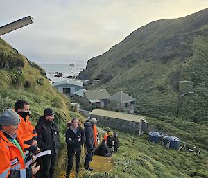 A line of people on steep stairs set against the side of a grassy hill with many buildings visible below them.