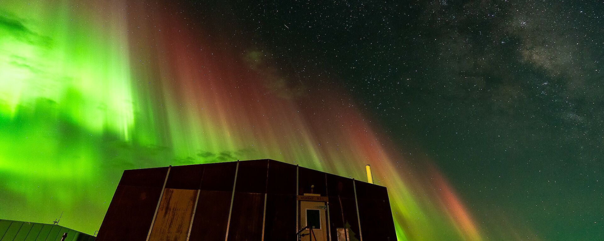 A shimmering green aurora australis over a hut