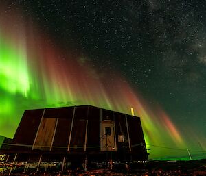 A shimmering green aurora australis over a hut