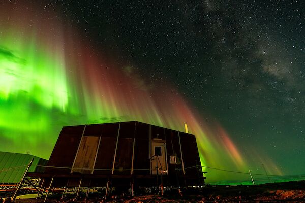 A shimmering green aurora australis over a hut
