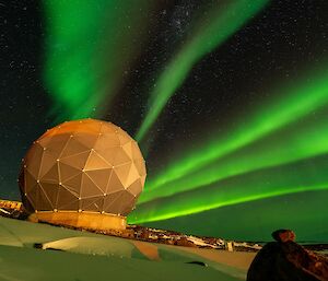 Streaks of green sky at night over a round satellite dome