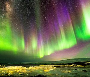 A curtain of green and purple light in the sky over snow