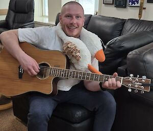 The soft toy goose sitting on the shoulders of an expeditioner who is playing guitar