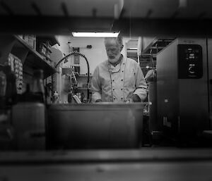 A bearded man wearing a chef's outfit preparing a meal - photo in black and white.