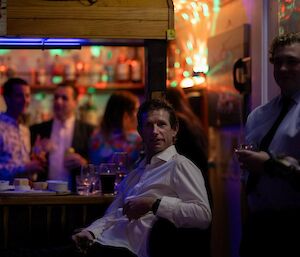 A smiling man looking very relaxed sits in front of a bar.