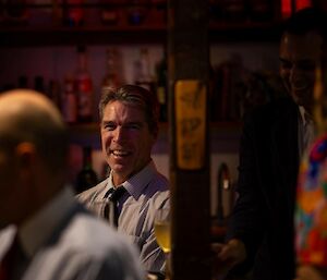 A smiling wearing a tie man sits behind a bar.