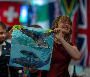 A smiling woman holds up a blue coloured piece of fabric with prints of whales on it.