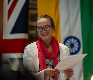 A smiling women wearing a pink scarf makes a speech at a dinner table.